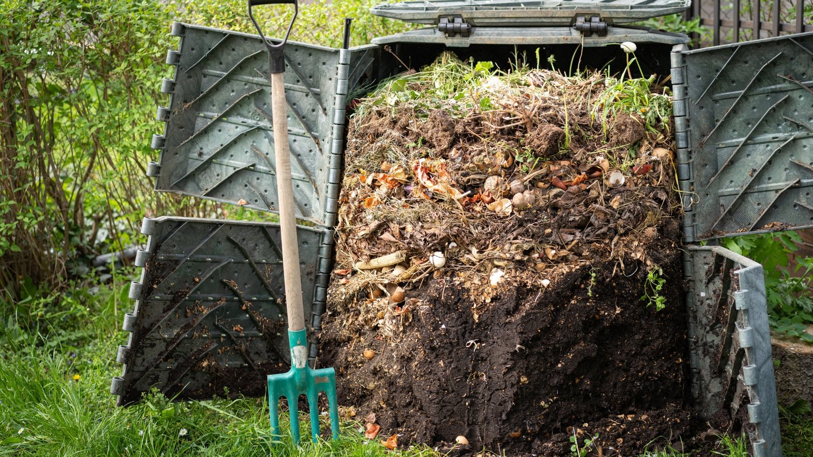 A close-up of layers of decomposing organic matter with different textures and colors inside a dark plastic bin.